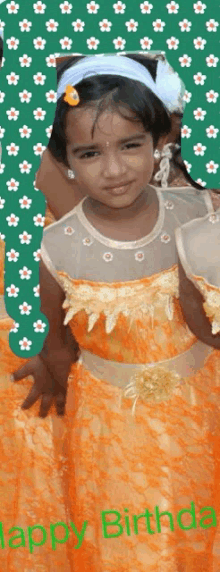 a little girl in an orange dress is standing in front of a happy birthday sign