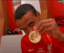 a man in a liverpool jersey is holding a gold medal in his hand .