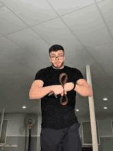 a man wearing glasses is holding a snake in his hands .