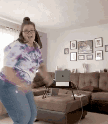 a woman in a tie dye shirt is dancing in a living room with a laptop on a table .