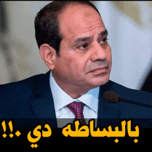 a man in a suit and tie stands in front of a microphone with arabic writing above him