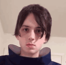 a young man with long hair is wearing a blue turtleneck sweater and looking at the camera .