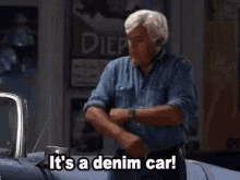 a man in a denim shirt is standing in front of a car and says it 's a denim car .