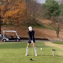 a woman is swinging a golf club on a golf course while a golf cart is parked in the background .