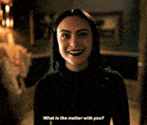 a woman in a black turtleneck is smiling and asking what is the matter with you
