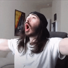 a man with long hair and a beard is wearing a hat and headphones while sitting in a chair .