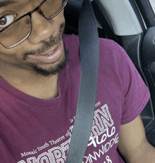 a man wearing glasses and a purple shirt that says mosaic youth theatre of pinwiddie