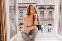 a woman is sitting on a window sill drinking coffee