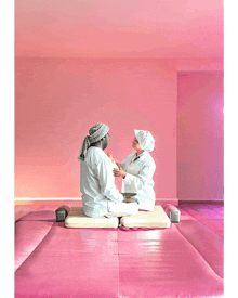 a man and a woman are sitting on a pink mat in front of a pink wall