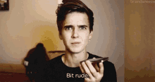 a young man is holding a cell phone and saying bit rude .