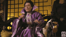 a man in a purple robe is sitting in a chair with a drink in front of him and a logo for psiots.com