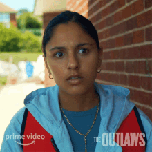 a woman stands in front of a brick wall with the words " the outlaws " on the bottom right