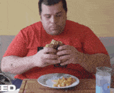 a man in a red shirt is sitting at a table with a plate of food and a glass of water with the word feed on the table