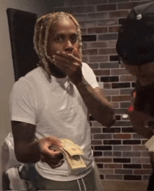 a man in a white shirt is holding a stack of money in front of his mouth .