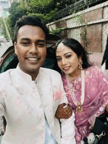 a man and a woman pose for a picture and the man is wearing a white jacket