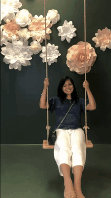 a woman sits on a swing in front of a wall of paper flowers