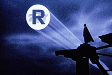 a silhouette of a man standing on top of a building in front of a circle with the letter r on it