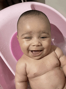 a baby smiles while taking a bath in a pink bathtub