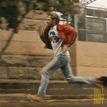 a man in a white shirt and red jacket is running down a street with fall out guy written on the sidewalk