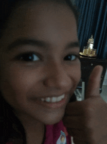 a young girl giving a thumbs up in front of a blue curtain