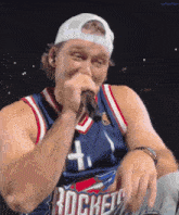 a man singing into a microphone wearing a rockets jersey