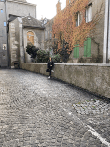 a woman sits on a stone wall in a cobblestone street