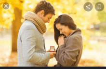 a man is giving a ring to a woman in a park