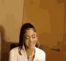 a woman wearing hoop earrings and a white shirt is sitting in front of a door and smiling .