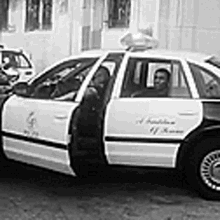 a black and white photo of a police car parked in front of a building with its doors open .