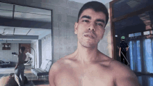 a shirtless man is taking a selfie in front of a mirror in a room .