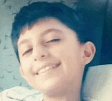 a young boy is smiling and looking at the camera while laying on a bed .