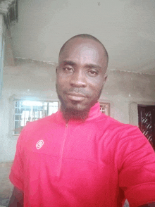 a man wearing a red shirt with a white logo on the front is taking a selfie