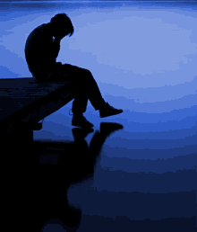 a silhouette of a person sitting on a dock with their head down