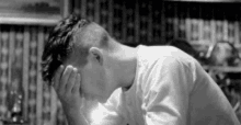 a black and white photo of a young man covering his face with his hands .