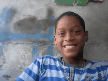 a young boy wearing a blue and white striped shirt is smiling for the camera