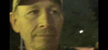 a man wearing a baseball cap is looking at the camera at night .