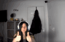 a woman wearing headphones is giving a thumbs up with the word oke behind her