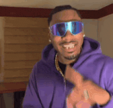 a man wearing sunglasses and a purple hoodie smiles