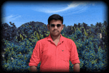 a man wearing sunglasses and a red shirt stands in front of a blue background