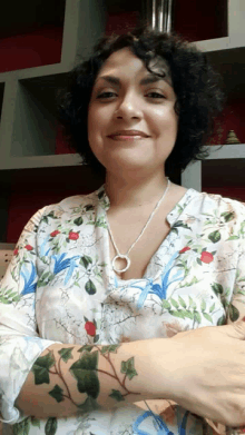 a woman with curly hair wearing a floral shirt and a silver necklace