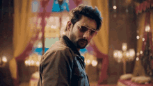 a man with a beard wearing sunglasses is standing in a room looking at the camera .