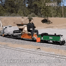 a man is sitting on a small train with the words " taking the train home " on the bottom