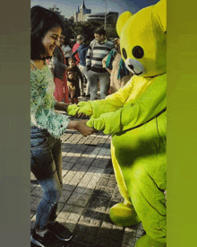 a woman is shaking hands with a yellow teddy bear mascot