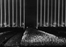a black and white photo of a crowd of people standing in front of a row of columns of lights .