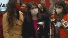 a group of women wearing face masks are standing in front of microphones with a sign that says aez in the background