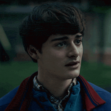 a close up of a young man 's face with a blue jacket on
