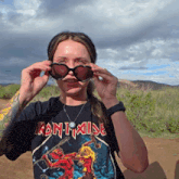 a woman wearing an iron maiden t-shirt is covering her eyes with sunglasses