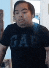 a man wearing a gap shirt is standing in a room .