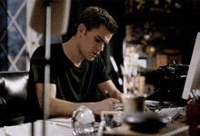 a man in a black shirt is sitting at a desk writing