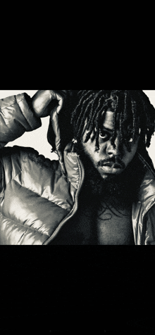 a black and white photo of a man with dreadlocks wearing a hooded jacket